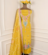 Yellow embroidered saree with floral decorations on a mannequin against a white wall.